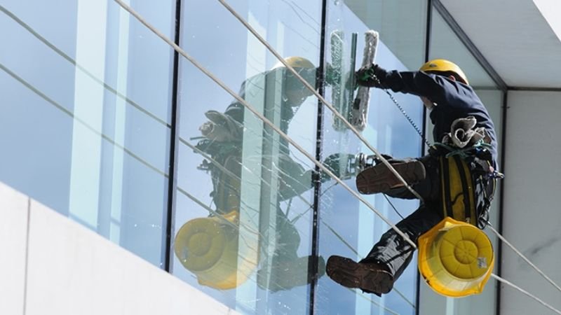 A man in a hard hat performs glass cleaning on a building, exemplifying a professional commercial window cleaning service.