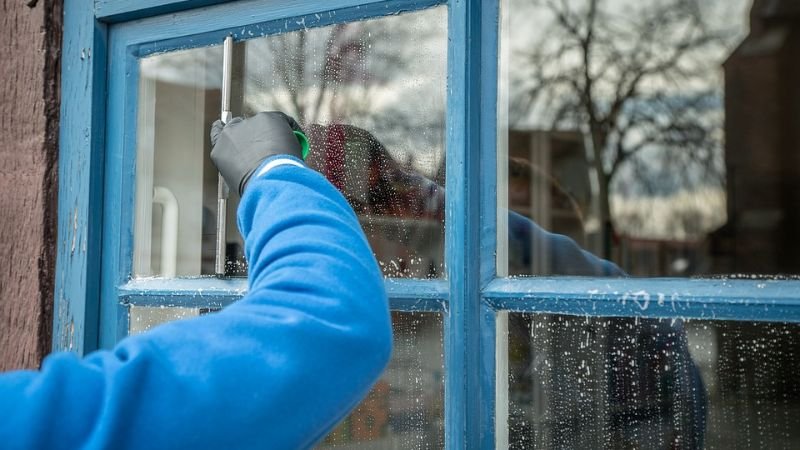 A person wearing blue gloves is seen cleaning a window, illustrating a domestic window cleaning service in action.