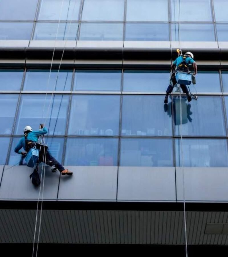 Two men using ropes to clean windows on a building, exemplifying the expertise of the Awning Window Cleaning Service.