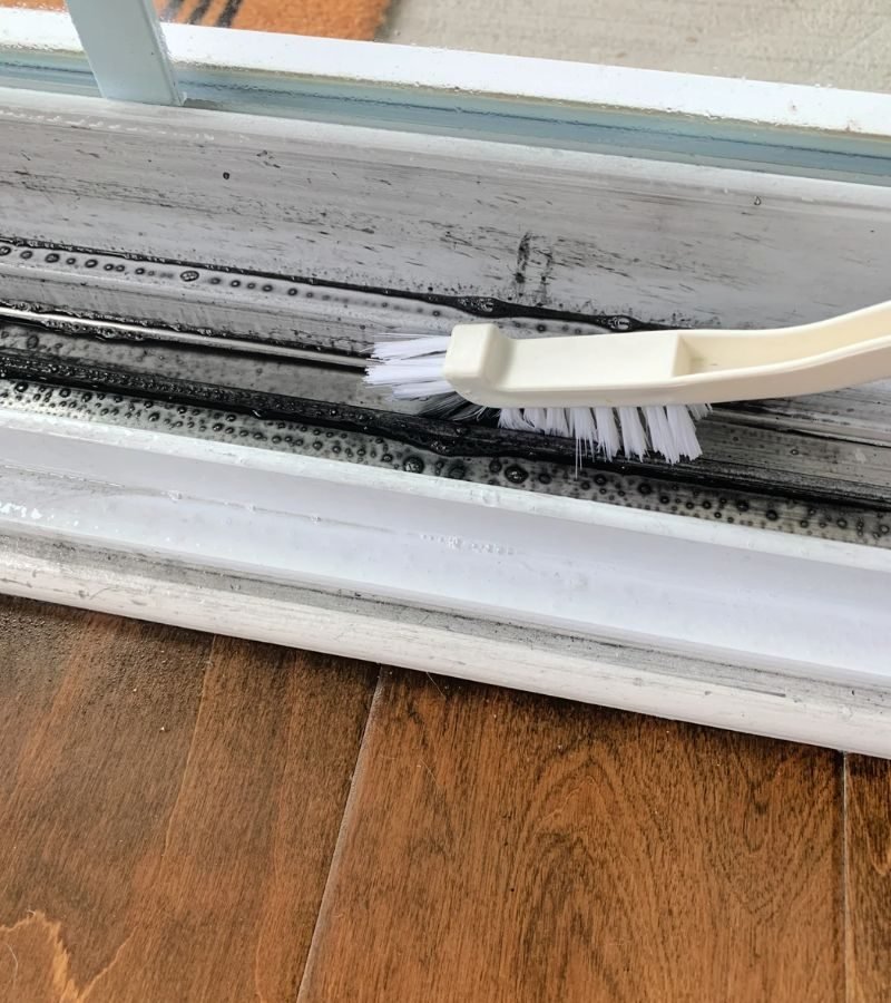 A white brush cleans a window, emphasizing the attention to detail in window track detailing services.